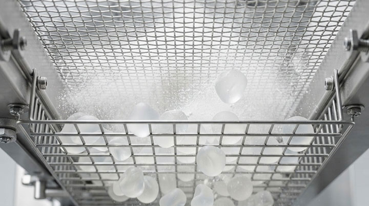 Close-up from beneath showing food-grade silicone bouncing elastomer balls striking the stainless steel screen mesh to prevent blinding in an industrial grading machine.