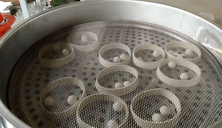 The internal self-cleaning system of a Dahan rotary vibrating screen, showing white bouncing elastomer balls beneath a tensioned wire mesh to prevent mesh blinding.