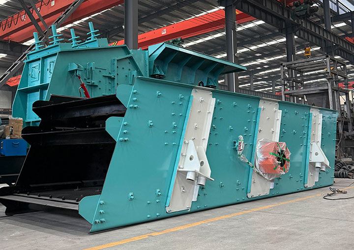 Heavy-duty elliptical vibrating screen with integrated spray bar system actively washing and separating wet, sticky ore in an aggregate processing plant.